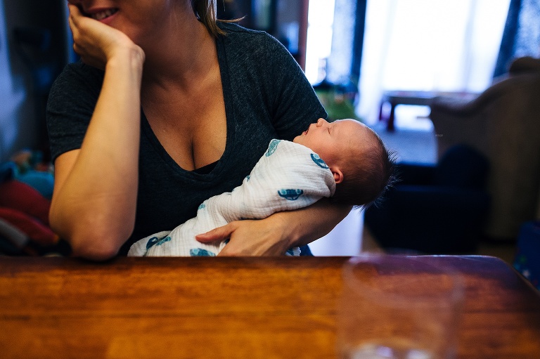 Mom sits at the table holding sleeping newborn baby.