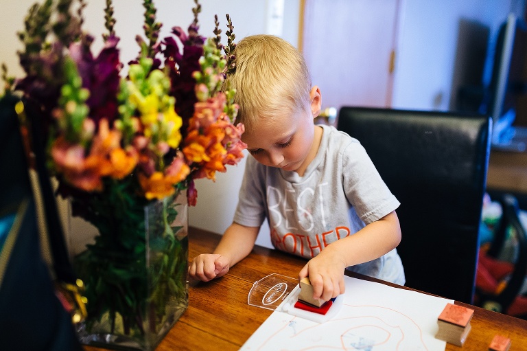 Young boy sitting at the table next to a bouquet of flowers stamps a piece of paper.