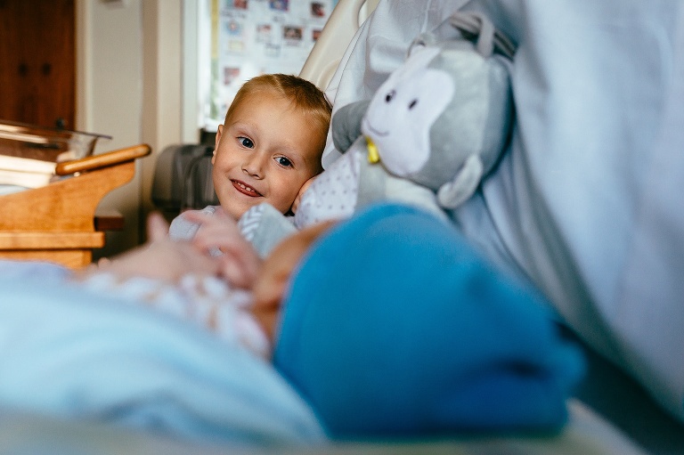 Young boy sits in the hospital bed next to his new baby brother.