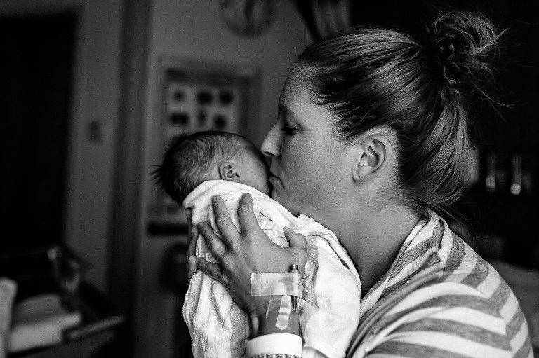 Black and white. Mom holding sleeping newborn baby up to her face. 