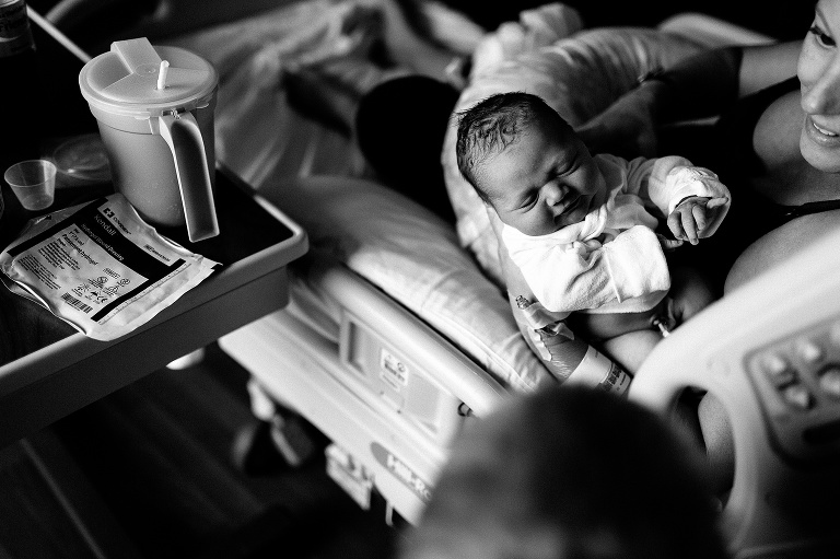 Black and white. Mom sitting in the hospital bed holds newborn baby.