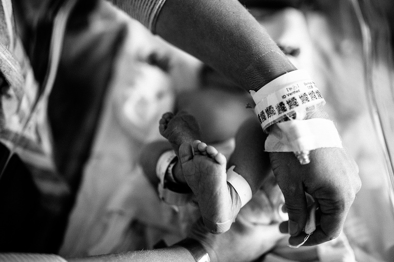 Black and white image. Mothers wrist with hospital tags. Newborn baby's ankles with hospital tags.