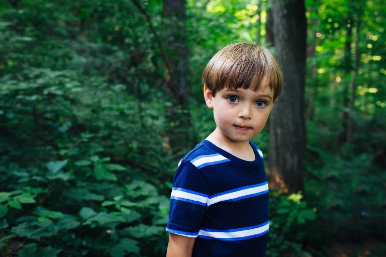 Young boy standing outside in the woods looking at the camera.