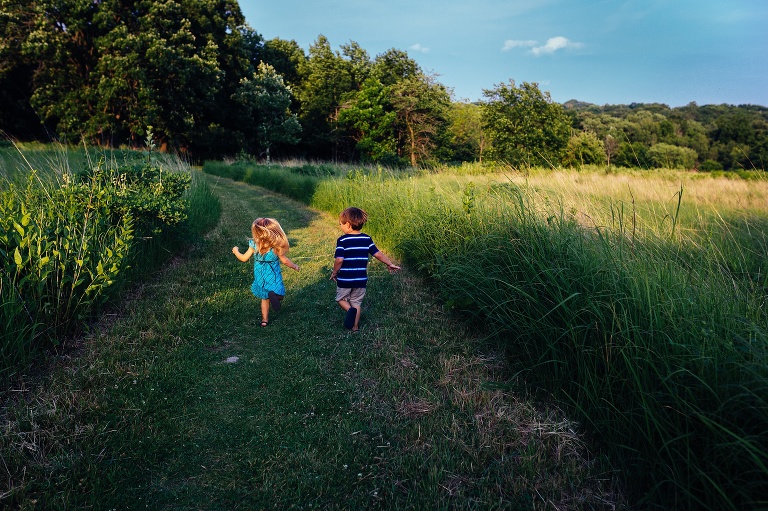 Young brother and sister run down a grassy path together.