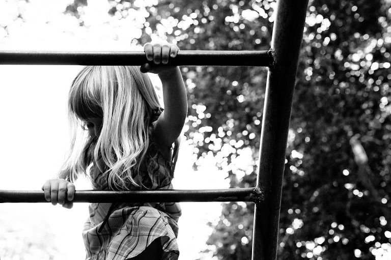 Black and white image. Young girl climbing down a ladder at a playground.