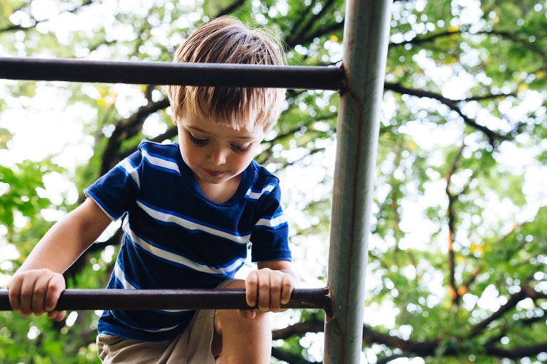 Young boy climbing up a ladder outside on a playground.