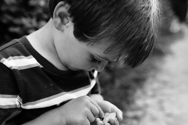 Up close black and white image. Young boy standing outside looking at things in his hand.