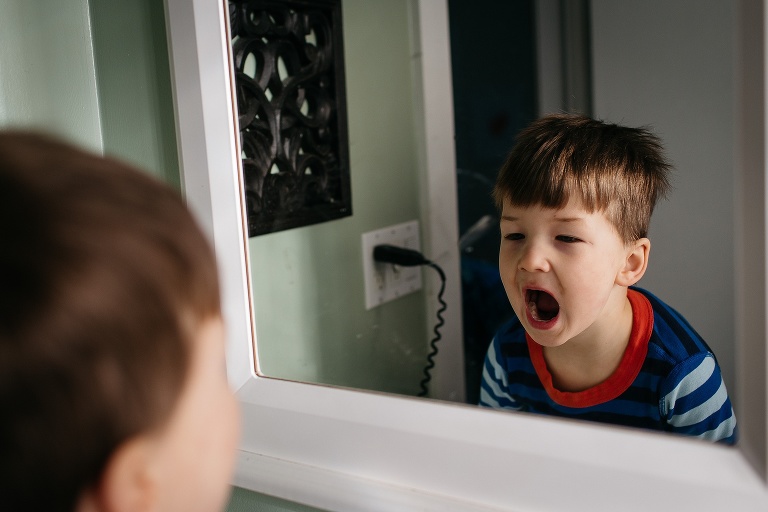 Young boy opens mouth and looks into bathroom mirror.