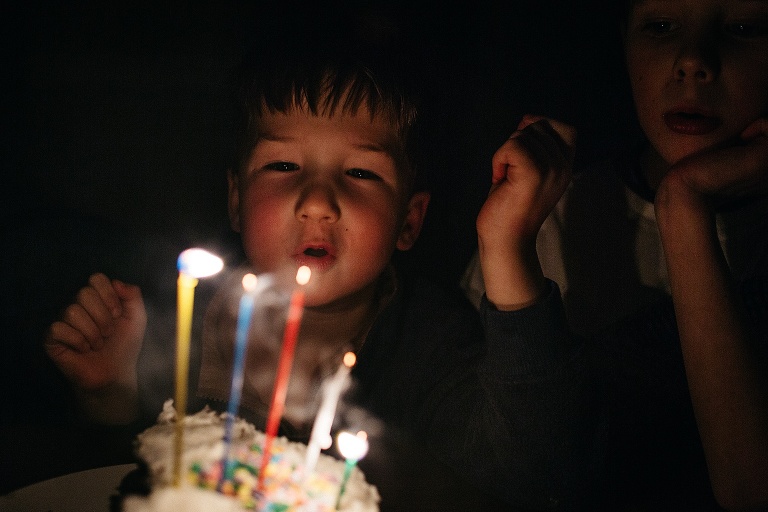 Young boy blows out candles on a cake celebrating his fourth and a half birthday.