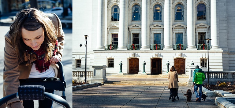 Mother pushes stroller as father walks two dogs down sidewalk downtown at christmas time.