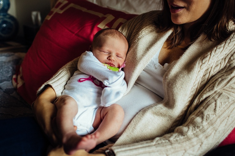 Mother lays on bed holding sleeping newborn baby.