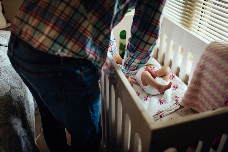 Father places newborn baby girl into crib.