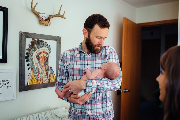 Mother smiles while watching father hold newborn baby girl.