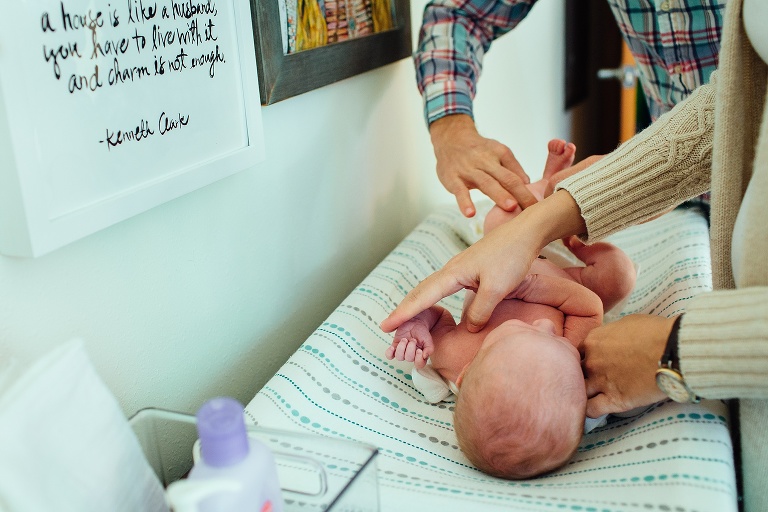 Mother and father change newborn baby laying on changing table.