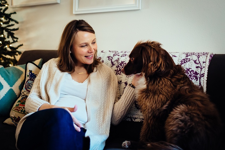 Woman sits on couch petting big brown dog.