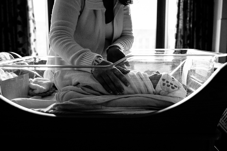 Black and white. Mother picks sleeping newborn baby up from the bassinet in the hospital.