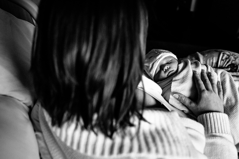Black and white. Mother lays in hospital bed holding sleeping newborn baby girl.