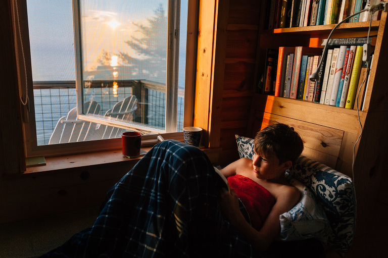 Boy reads in a window seat near lake and sunset