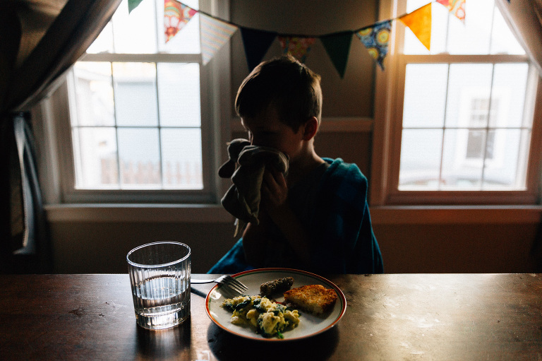 Young boy holds small lovey to face while his dinner goes untouched. 