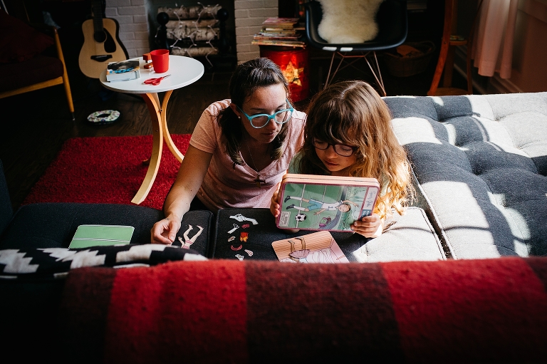 Mother and daughter read books over on the floor of a living room. 