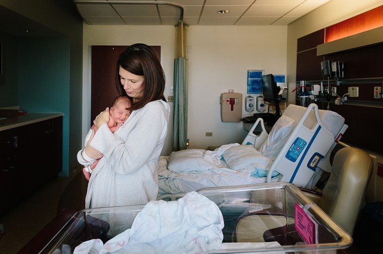 New mother holds newborn in an embrace against her chest in a hospital room.