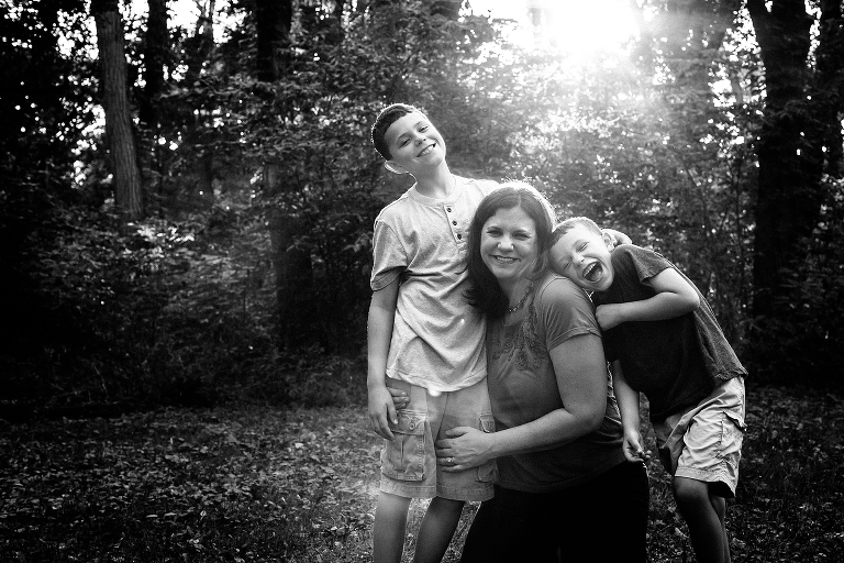 Black and white. Mom smiles with her two boys leaning on her with lots of sun flare. 
