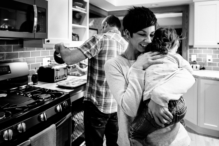 Mother holds young daughter in impromptu hug in the kitchen. 