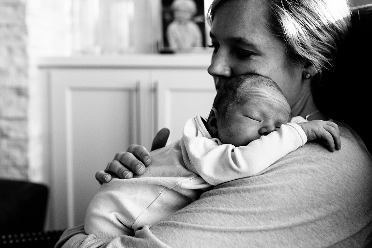 Black and white. Mother holds newborn baby over her shoulder.
