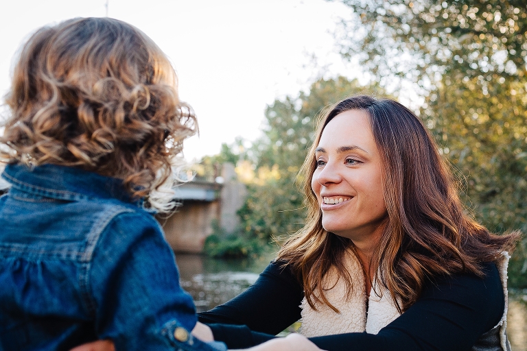 Focus of mother smiling at her preschool age daughter in beautiful light. 
