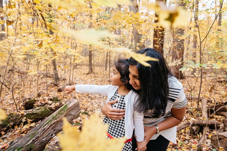 Daughter points out into a forest of yellow leaves while her mother has her arm around her 