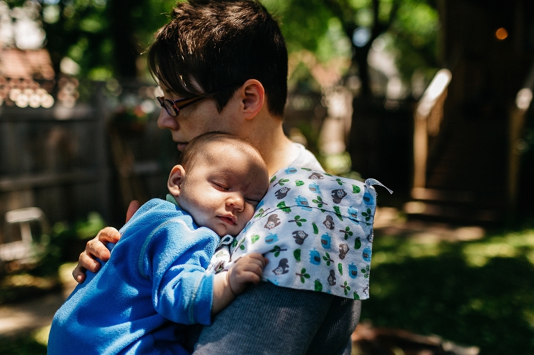 Mom holds newborn in the backyard with summertime dappled light. 