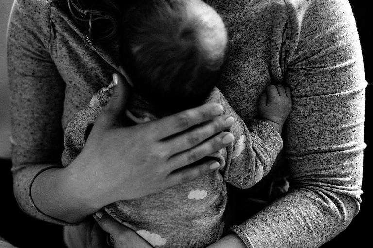 Black and white. Mother holds newborn baby on her chest.