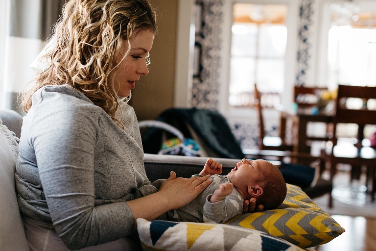 Mother sits on the couch holding newborn baby.
