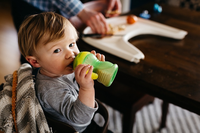 Baby boy sits at table drinking a bottle of milk.