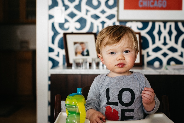 Little boy sitting in high chair with a bottle of milk.