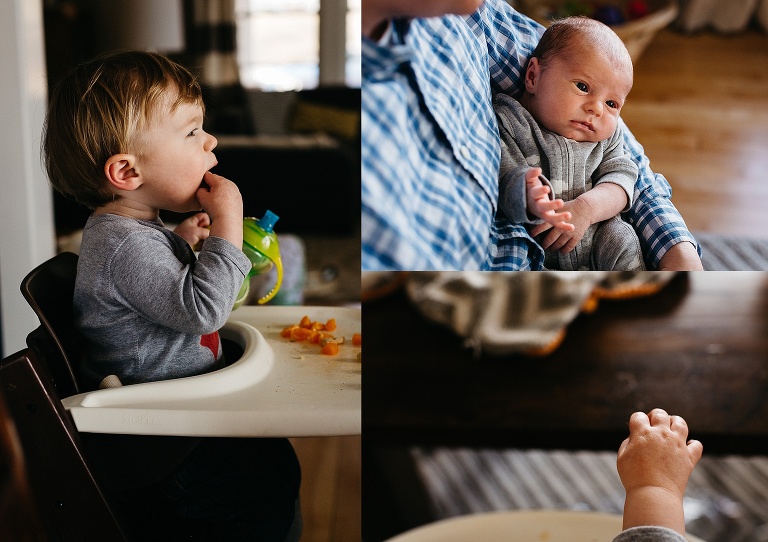 Little boy sitting in high chair eating a snack while newborn gets held by father.