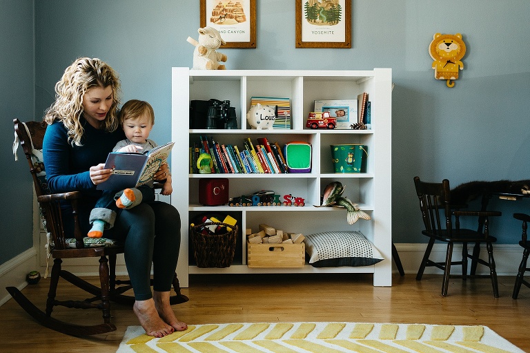 Mother sits in wooden rocking chair with son in her lap reading a picture book.