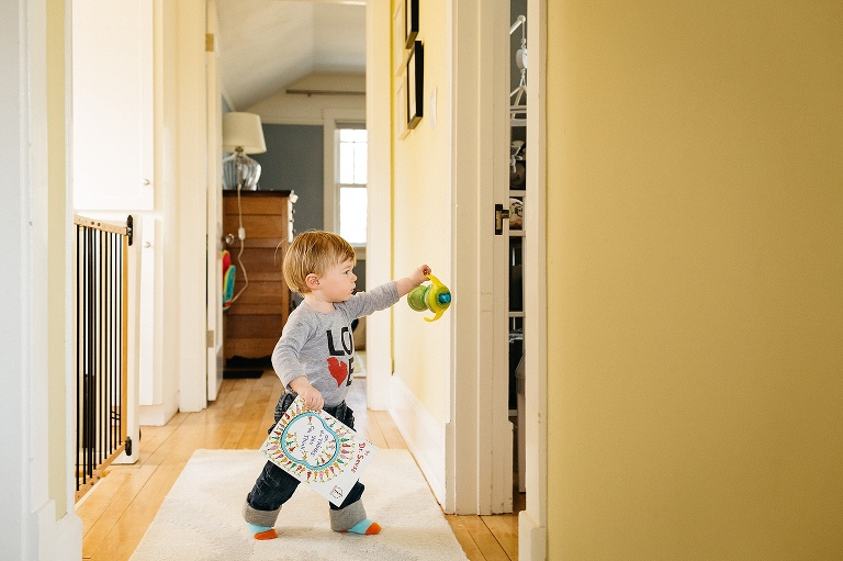 Little boy walks around the house carrying bottle and picture book.