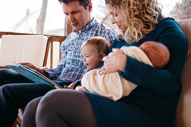 Mother and father read a picture book to toddler and newborn.