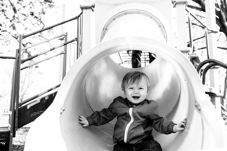 Black and white. Toddler boy goes down slide at park playground.