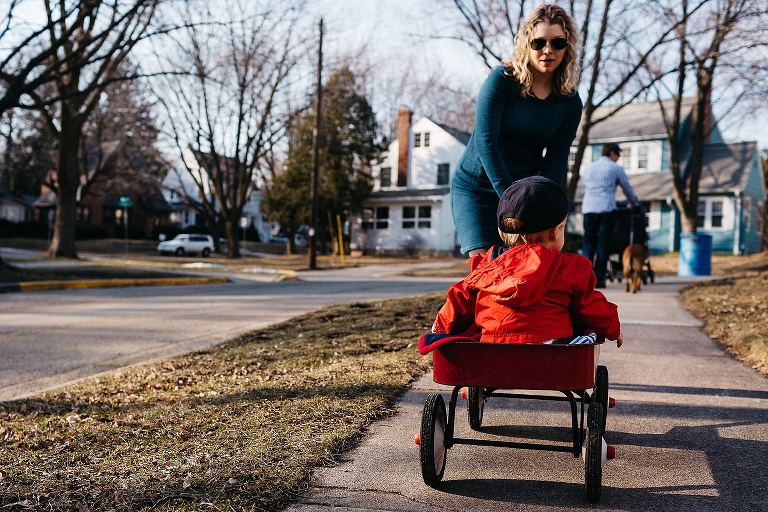 Family walks down sidewalk. Mother pulling son in wagon.