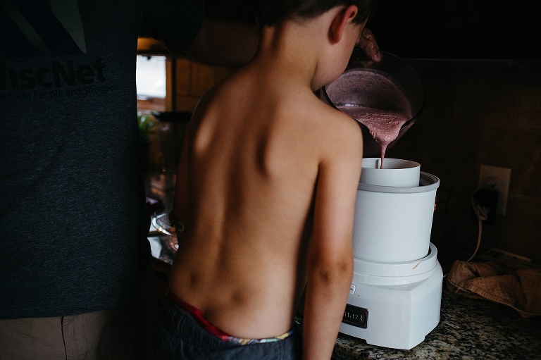 Young shirtless boy watches as strawberry mixture gets poured into ice cream maker.