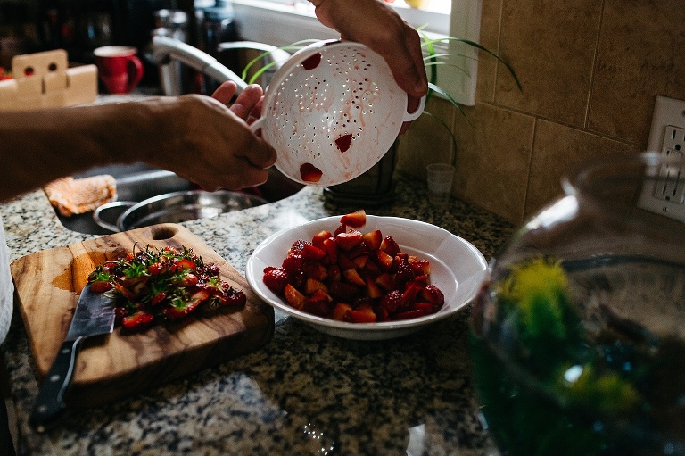 Sliced strawberry's being placed into a bowl on kitchen counter.
