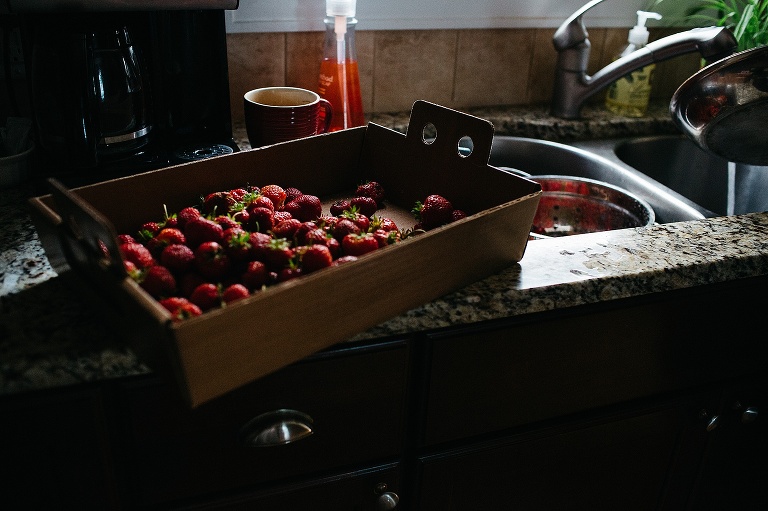Carton full of strawberry's sitting on kitchen counter next to the sink.