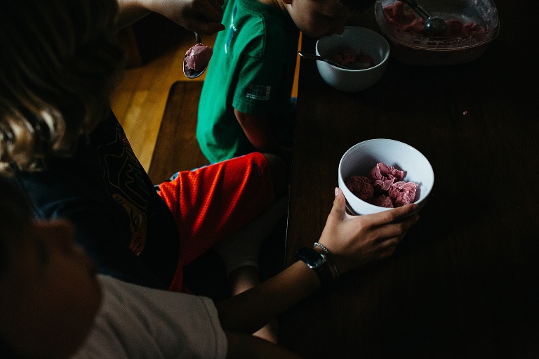Boys sitting at kitchen table eating strawberry ice cream.