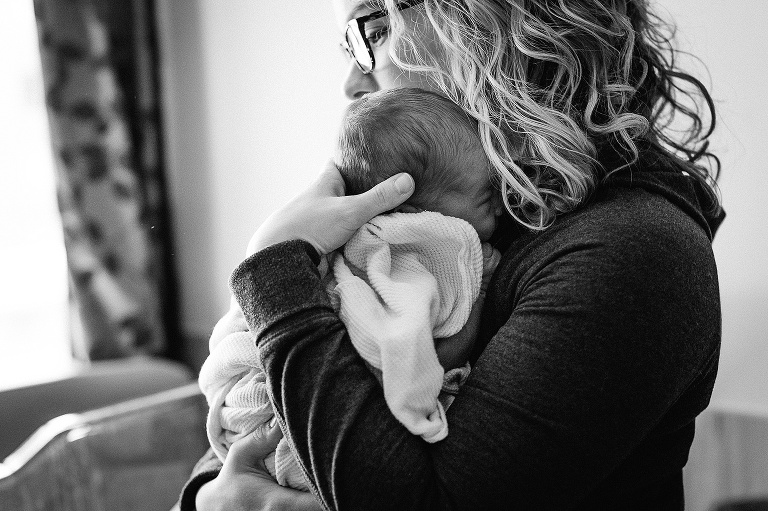 Black and white. Mother holds sleeping newborn baby up to her chest.