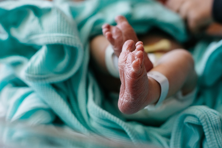 Newborn baby's wrinkled feet hospital tags on baby's ankles.