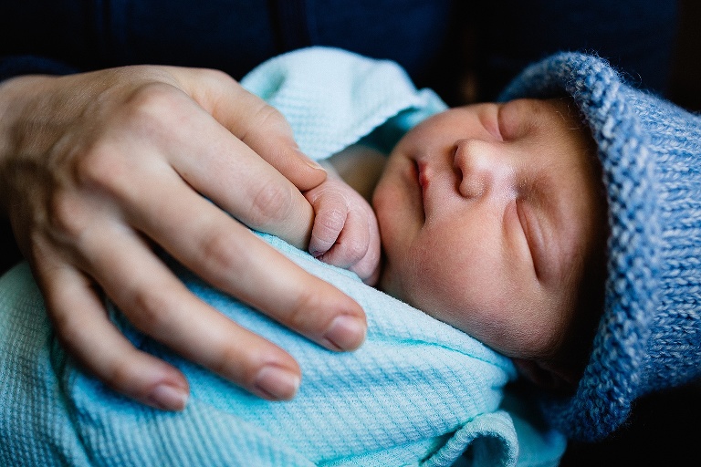 Sleeping newborn baby holds mothers finger.