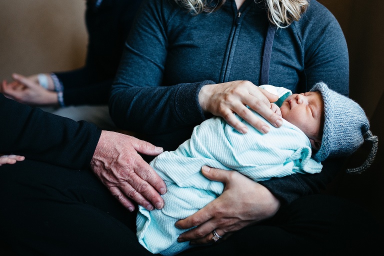 Mother sitting while holding swaddled and sleeping newborn baby in the hospital.