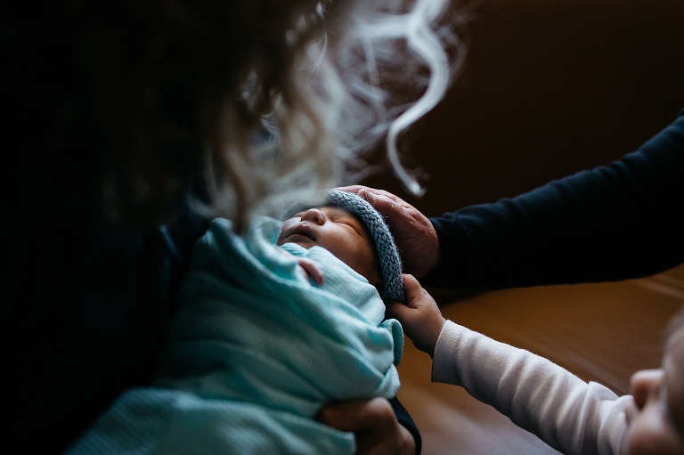 Mother, father, and son look at sleeping newborn baby.
